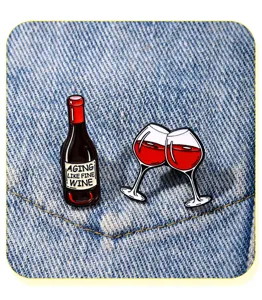 Primo piano di bottiglia di vino rosso e bicchieri spille smaltate, spilla in metallo su denim.