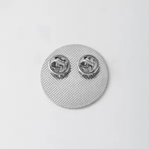 Metal badge back view showing dual butterfly clutch pins and grid texture for clothing accessory.