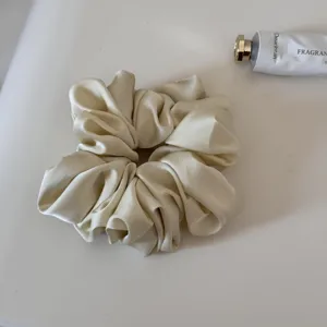 Close-up of a smooth satin hair scrunchie in cream color, gentle for daily styling.