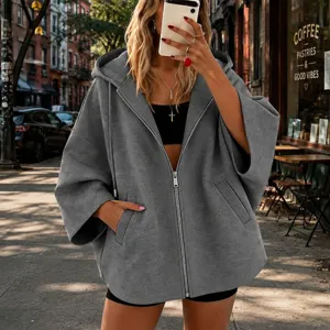 Detalle de sudadera con capucha gris con cremallera, mangas murciélago, escena de estilo urbano.