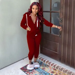 Detail shot of the burgundy hooded tracksuit worn by model in outdoor entrance setting.