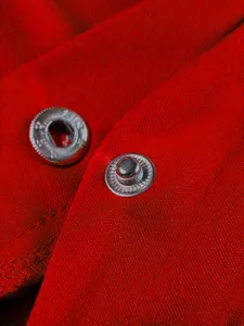 Primo piano dei bottoni a pressione metallici della giacca rossa, con trama di tessuto fine.
