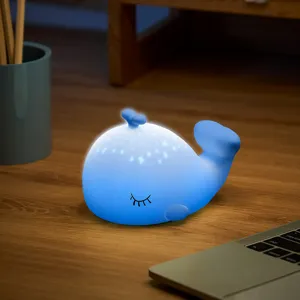 Gros plan de la veilleuse baleine en silicone bleue lumineuse sur le bureau en bois.