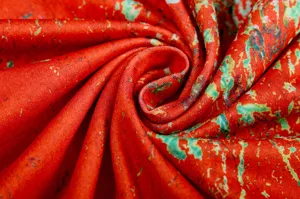 Close-up detail of vibrant red abstract printed fabric with green and golden spots texture.
