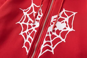 Détail d'un sweat à capuche rouge zippé avec un imprimé cœur en toile d'araignée blanche.
