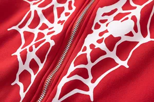 Gros plan détail du sweat à capuche rouge avec impression toile d'araignée blanche et zip métal.