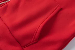Gros plan sur la poche et la fermeture éclair du sweat à capuche rouge, texture douce.