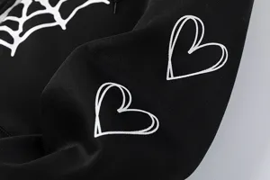 Gros plan détail du sweat à capuche noir en polaire avec impression toile et cœurs.