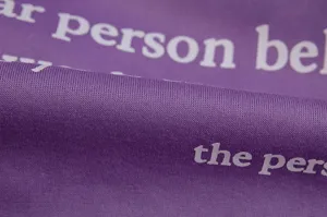 Close-up detail of purple fleece hoodie fabric featuring stylish white letter print texture.