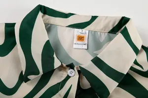 Gros plan détail du col et du bouton de chemise à manches longues imprimé abstrait vert.
