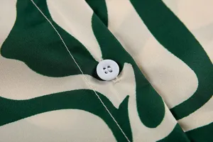 Gros plan détaillé d'une chemise chic à imprimé abstrait vert avec boutons blancs.