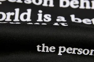 Close-up detail of black fleece hoodie fabric featuring crisp white letter printing texture.