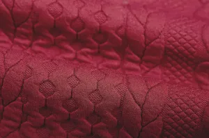 Detailed shot of dark red jacquard fabric with geometric diamond and grid patterns.