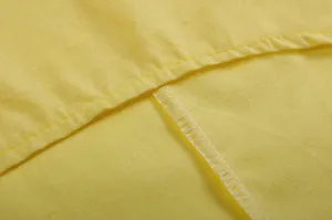 Gedetailleerde close-up van de overlockzomen en het vakmanschap van een geel katoen-linden kledingstuk.