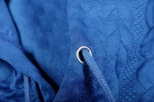 Blue jacquard hoodie detail close-up showing metal eyelet and braided drawstring texture.