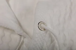 Close-up detail of white jacquard fabric, metal eyelet and drawstring on casual hoodie.