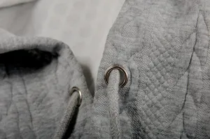 Grey jacquard hoodie detail view showcasing the textured fabric, metal eyelets and drawstring.