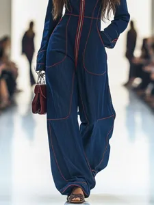 Detailed view of dark blue denim jumpsuit featuring red contrast stitching and front zipper.