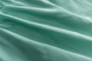 Λεπτομερές κοντινό πλάνο της υφής πράσινου υφάσματος, που δείχνει απαλές πτυχώσεις και λεπτή ύφανση.