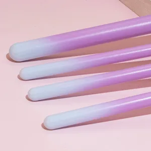 Close up view of purple and blue gradient makeup brush handles on pink background detail shot.