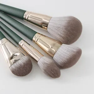 Close-up detail of soft makeup brush set with green handle and golden ferrule for smooth application.