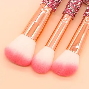 Close-up of rhinestone makeup brushes with soft pink gradient bristles and rose gold ferrule.