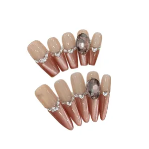 Lange künstliche Nägel, Nude-Basis, bronzefarbener Katzenauge-Effekt, Strass und große Kristalle.