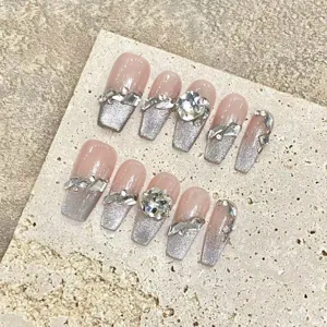 Gros plan d'ongles press-on faits main avec dégradé de paillettes argentées et strass.