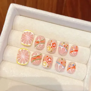 Faux ongles faits à la main avec des tranches d'agrumes et points colorés pour l'été.