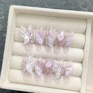 Kit d'ongles press-on faits main avec dégradé rose et ailes de papillon 3D blanches brillantes.