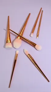 Set of 7 professional makeup brushes with rose gold diamond handles and soft pink bristles.