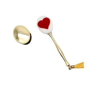Detailansicht des ovalen Make-up-Pinsels mit rotem Herzmuster, Goldgriff und Quaste.
