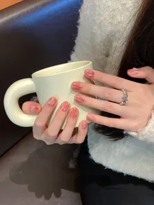 Close up detail of handmade press on nails featuring pink marble design held by model.