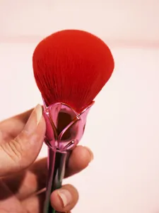 Close up detail of red fluffy powder makeup brush featuring metallic pink rose flower handle.