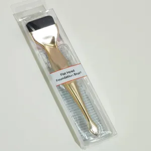 Detail view of the flat head foundation brush with gold handle in clear packaging.