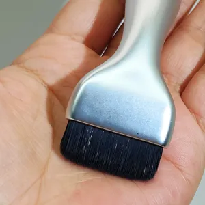 Close-up of flat spatula foundation brush with silver handle and dense black bristles.