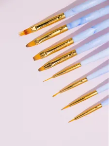 Close-up of professional nail art brush set showing fine tips, gold ferrules and marble handles.