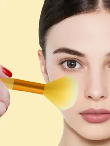 Detailed view of soft yellow makeup brush with wooden handle for face makeup application.