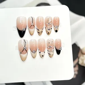 Set di unghie finte fatte a mano con base nude, punte nere, strass e decorazioni.