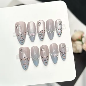 Unghie finte fatte a mano con stampa leopardata, fiocchi e strass, dettaglio di stile elegante.