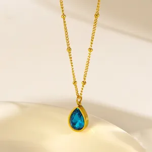 Close-up of a delicate gold-plated beaded chain necklace featuring a stunning blue teardrop pendant.
