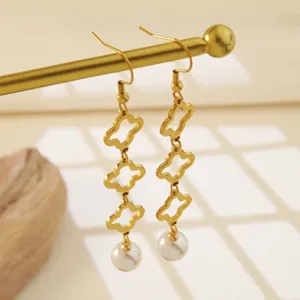 Detalle en primer plano de pendientes colgantes de trébol de acero inoxidable dorado.