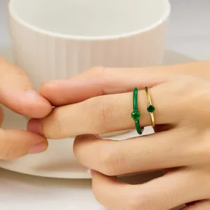 Detailed close-up shot of green heart enamel ring and gold zircon ring worn on finger.