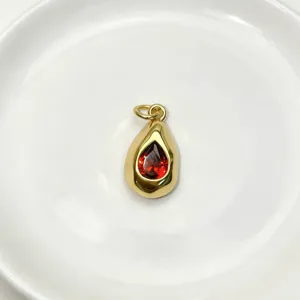 Detail shot of a teardrop metal pendant featuring a vibrant red gemstone center, elegant jewelry.