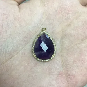 Detailansicht eines tropfenförmigen violetten Steinanhängers mit Zirkonrand in Goldoptik.