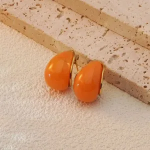 Detailed close-up of trendy orange teardrop earrings with gold trim on textured stone surface.