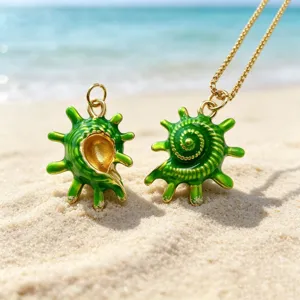Detailed close-up view of green enamel seashell pendant with gold accents on sand.