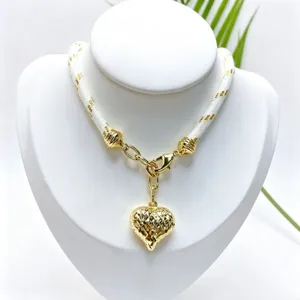 Close up detail of a gold heart pendant necklace with white woven chain on display bust.
