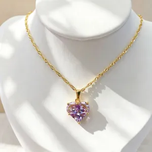 Gros plan d'un collier chaîne doré orné d'un pendentif en zircone cubique cœur mauve clair.
