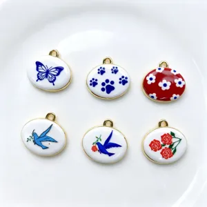 Primer plano de dijes ovalados de esmalte con diseños de mariposa, golondrina y rosas, borde dorado.